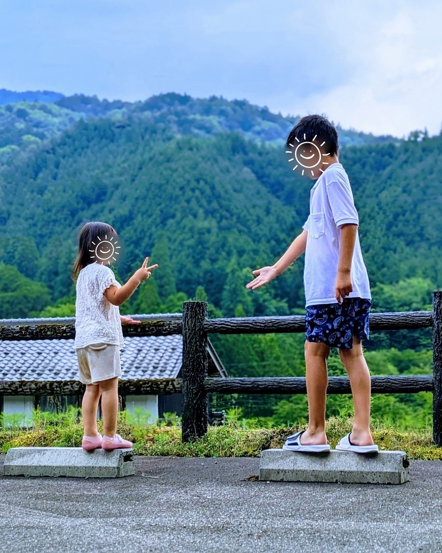 元の写真:川遊びの帰り道、車止めの上でじゃんけんをする2人(顔はスタンプで隠しています)
